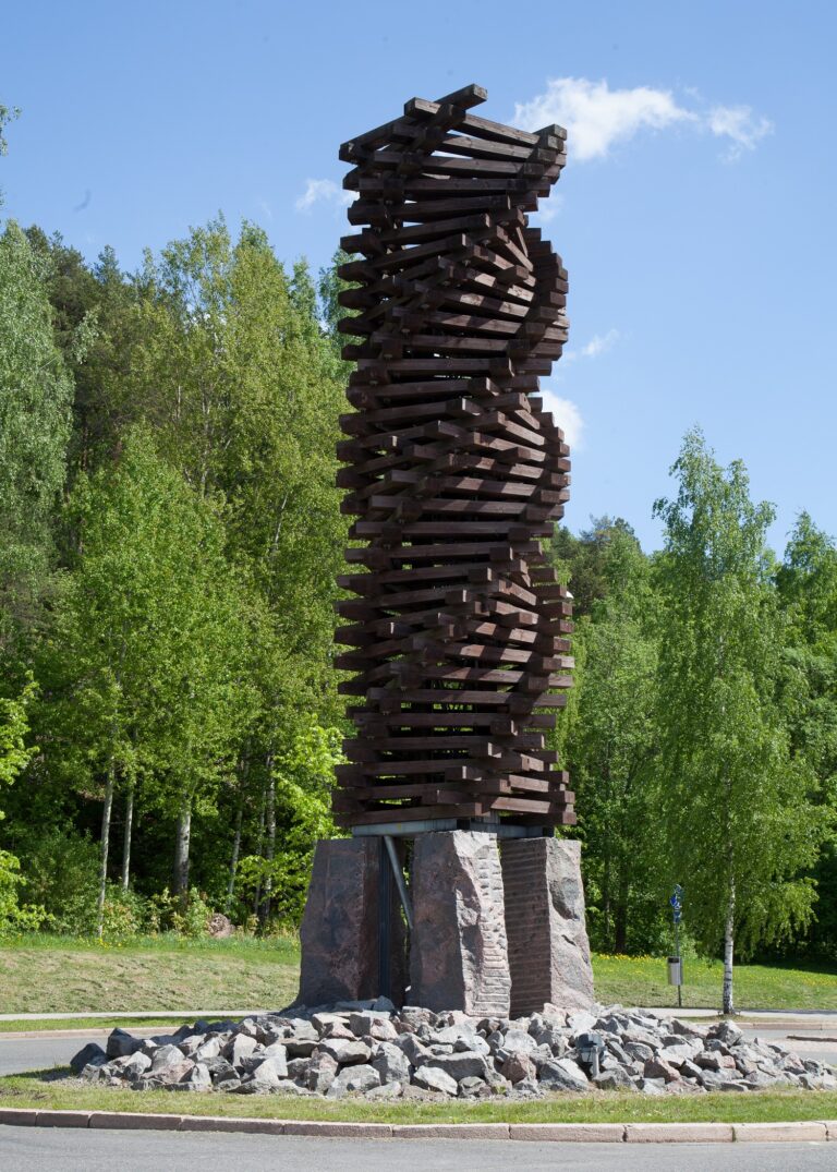 A spiral sculpture made of logs rising on top of four stone slabs.