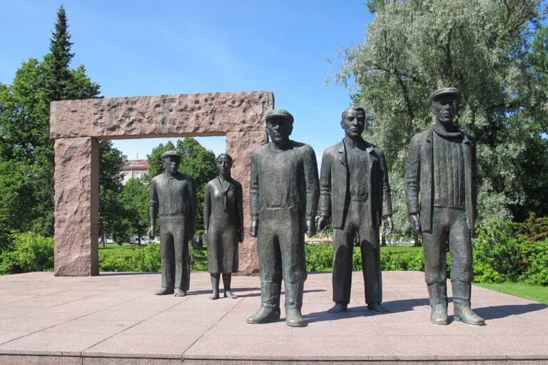 Five bronze human statues standing in workers' clothes in front of a gate-like structure.