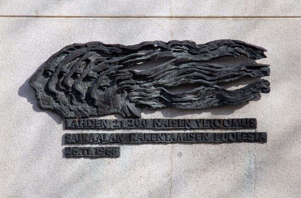 A bronze relief depicting the side profiles of five long-haired women.