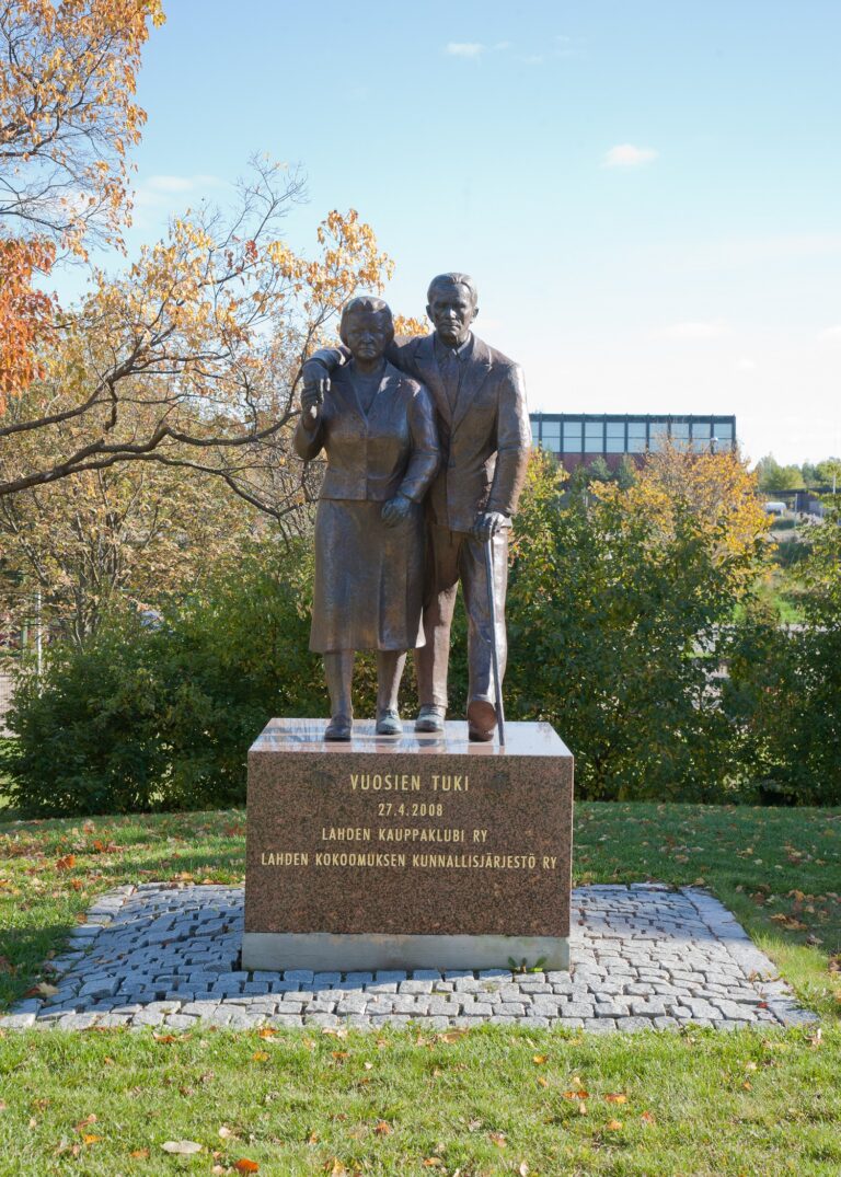 Bronze sculpture depicting a man leaning on a walking stick and holding hand on a woman's shoulders.