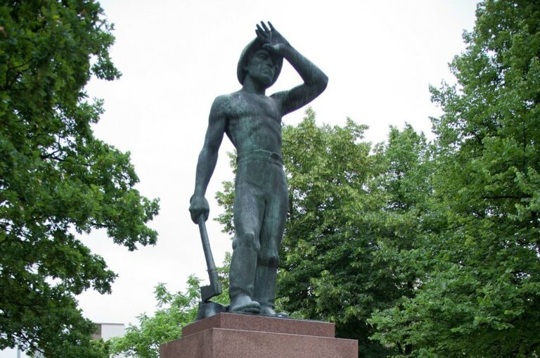 A bronze sculpture depicting a man wiping sweat from his forehead while holding an ax in other hand.