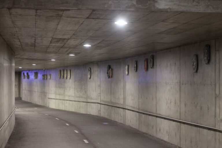 A tunnel with concrete reliefs depicting human faces attached to the wall.