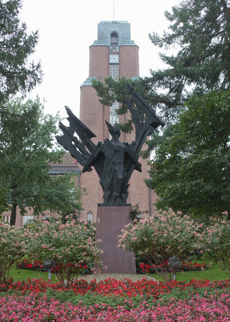 A sculpture with a human figure with arms spread out to the side, abstract shapes in the background.