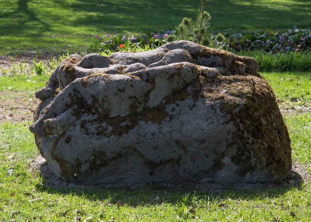 A concrete sculpture placed in the park depicting three human figures resting on a rock.