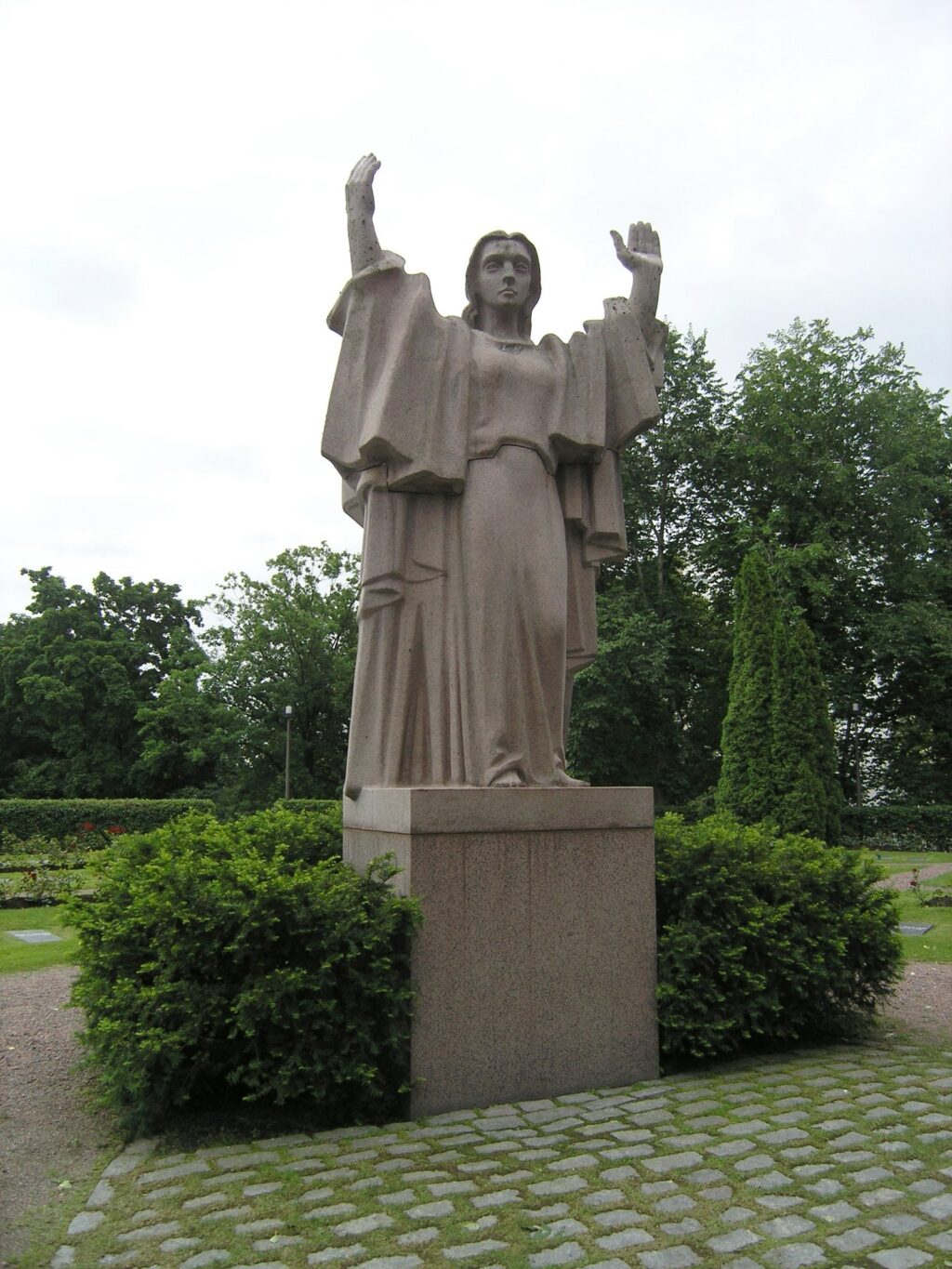 A red granite sculpture depicting a female figure standing with her hands up.