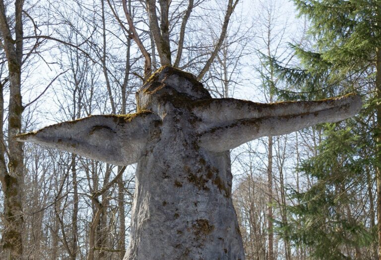 A concrete sculpture placed in the park, which depicts a human figure plunging through a high, upwardly narrowing stone block in a transverse direction.