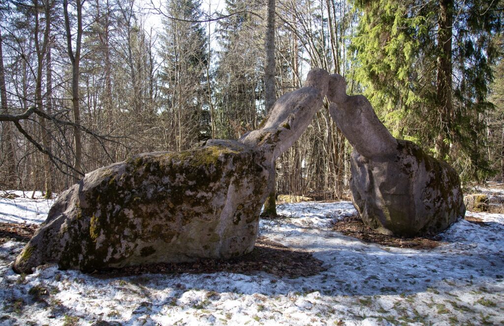 Puistoon sijoitettu betoninen veistos, joka kuvaa kahta kivenlohkareista nousevaa ja toisiaan kohti kurottautuvaa ihmishahmoa.