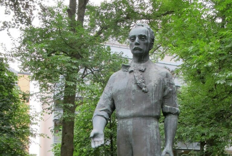 A bronze statue depicting a man holding a book in one hand and extending the other hand forward.