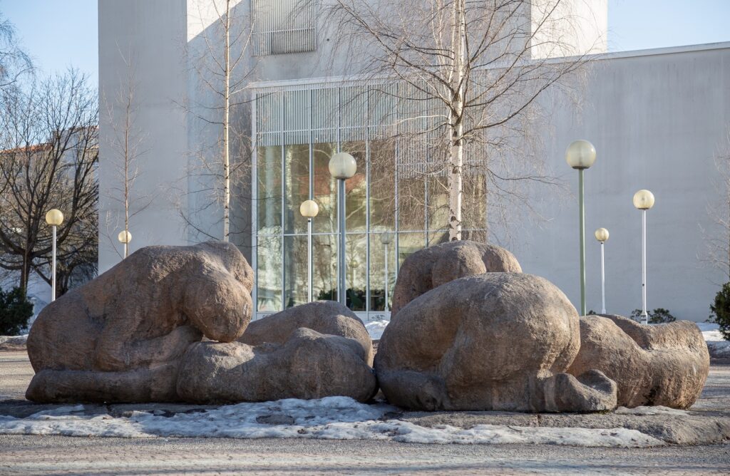 A set of concrete sculptures placed in front of the building, depicting five human figures in different positions against the ground.