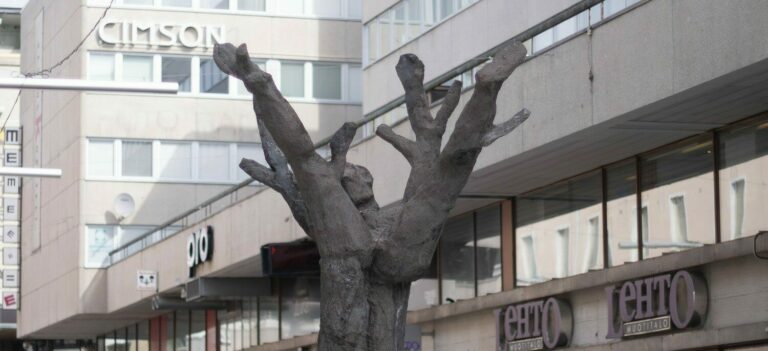 A concrete sculpture placed on the street depicting a human figure lying on a tree trunk.