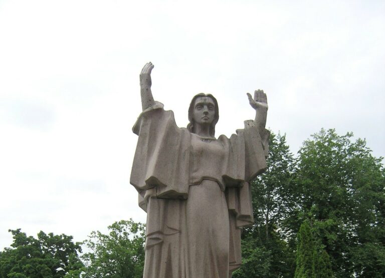 A red granite sculpture depicting a female figure standing with her hands up.