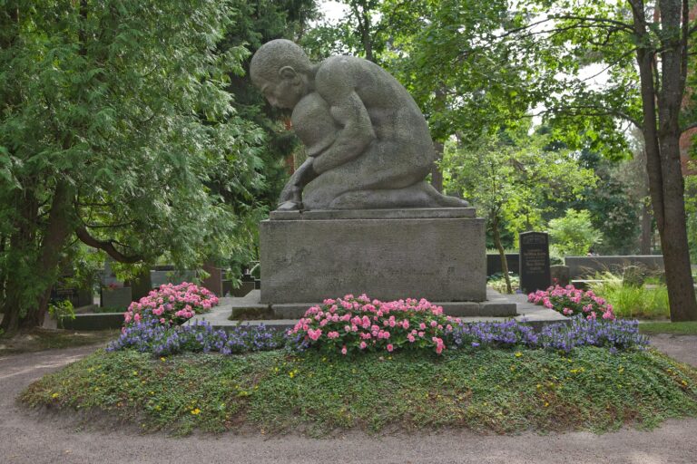 A statue depicting a kneeling man holding a helmet against his chest and lowering a sword to the ground.