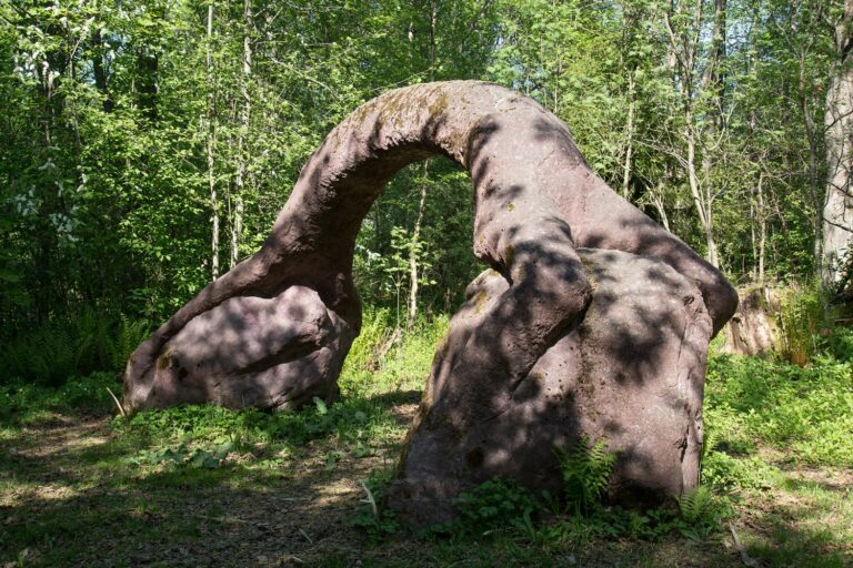 A concrete sculpture placed in the park, which depicts a human figure sitting on top of two stones in an arched, bridge-like position.