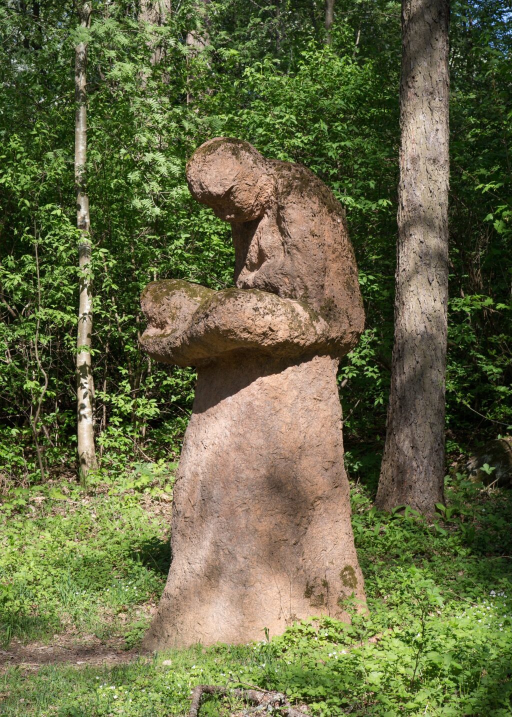 A concrete sculpture placed in the park depicting a human figure sitting on an anthill with their legs crossed.