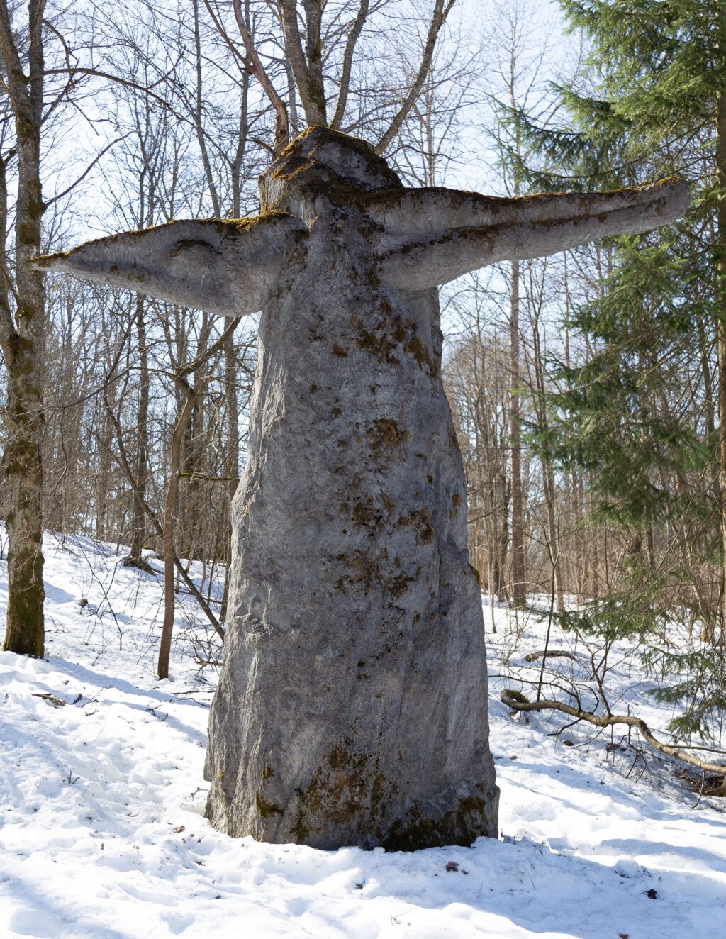 A concrete sculpture placed in the park, which depicts a human figure plunging through a high, upwardly narrowing stone block in a transverse direction.