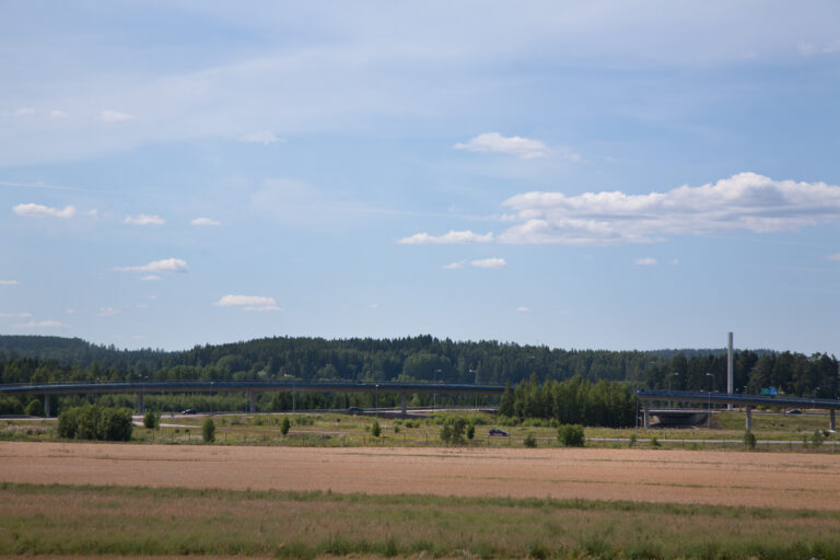 A field landscape with a bridge ramp visible in the background. The railing of the bridge glows blue.