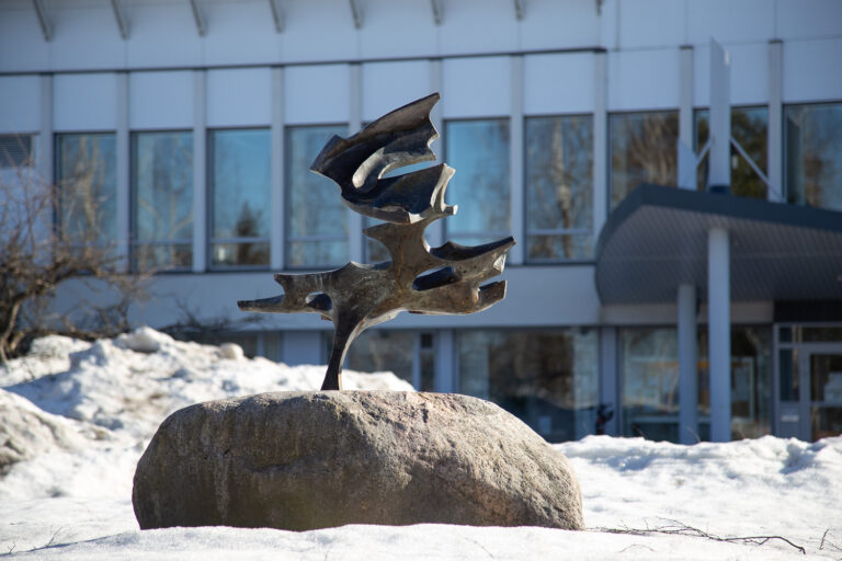 A bronze, abstract sculpture with a natural stone base.