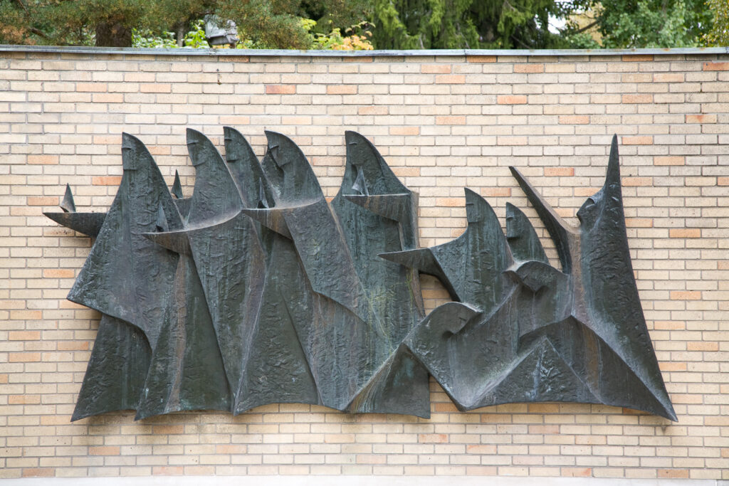 A bronze relief attached to a brick wall depicting ten female figures walking in a row.