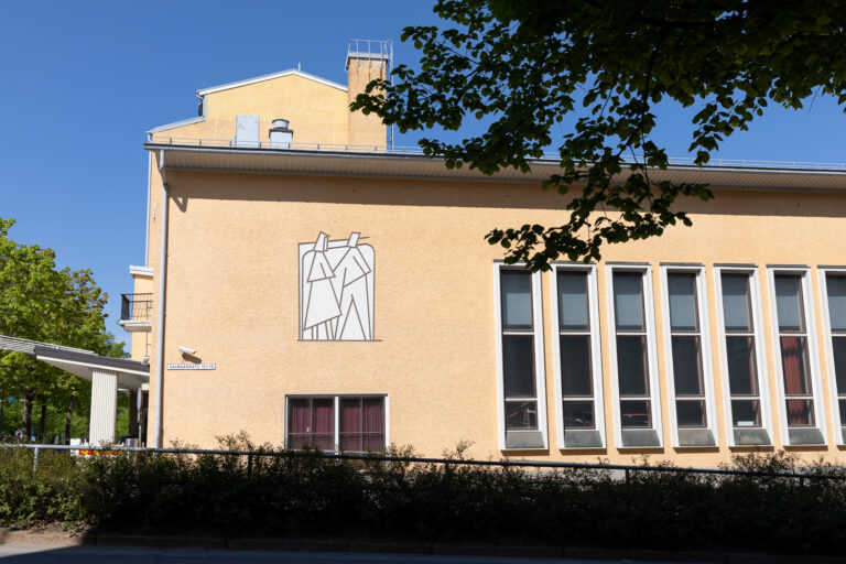 A motif implemented on the wall of the building with two angular human figures moving forward sideways and holding each other's hands.