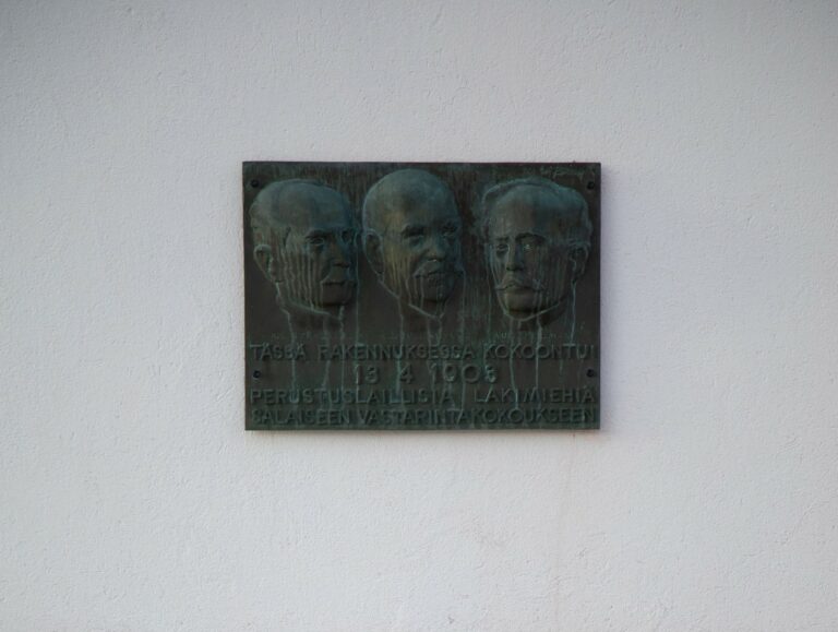 A relief with the faces of three men and a text attached to the wall of the building.