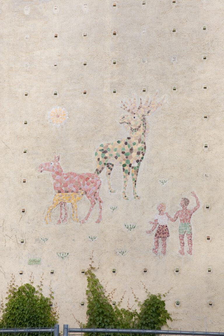 A mosaic relief attached to the facade of the building, depicting a family of deer and two children watching them.