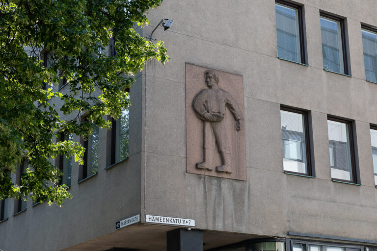 Stone relief on a building's wall depicting a person carrying a container.