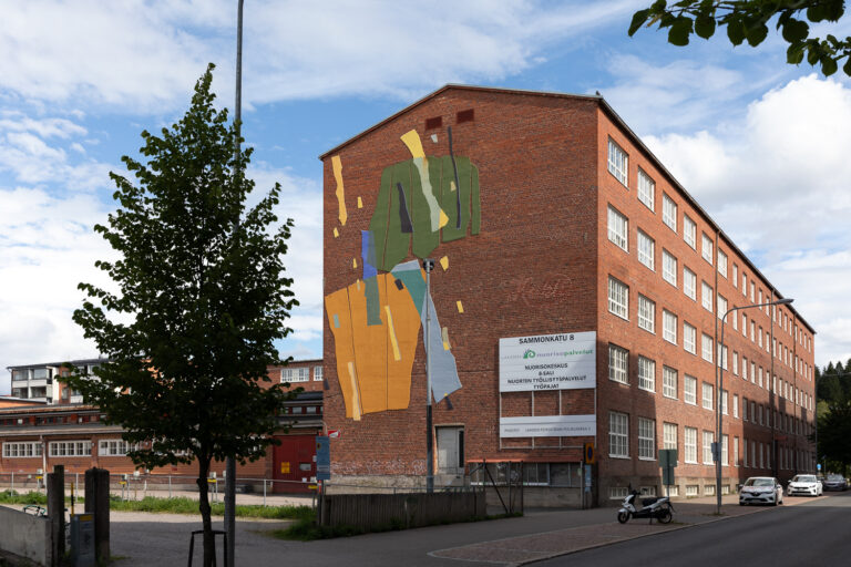 Brick building along the street with a colorful mural on its wall.