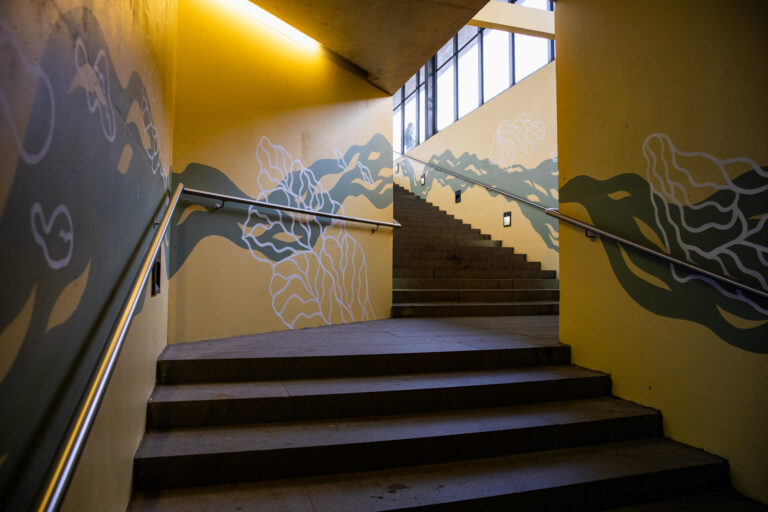 Staircase with yellow walls. Blue wavy patterns and white designs resembling marine plants painted on the walls.