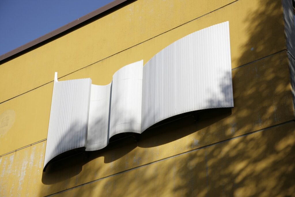 A three-dimensional, wave-like work attached to the outer wall of a yellow building.