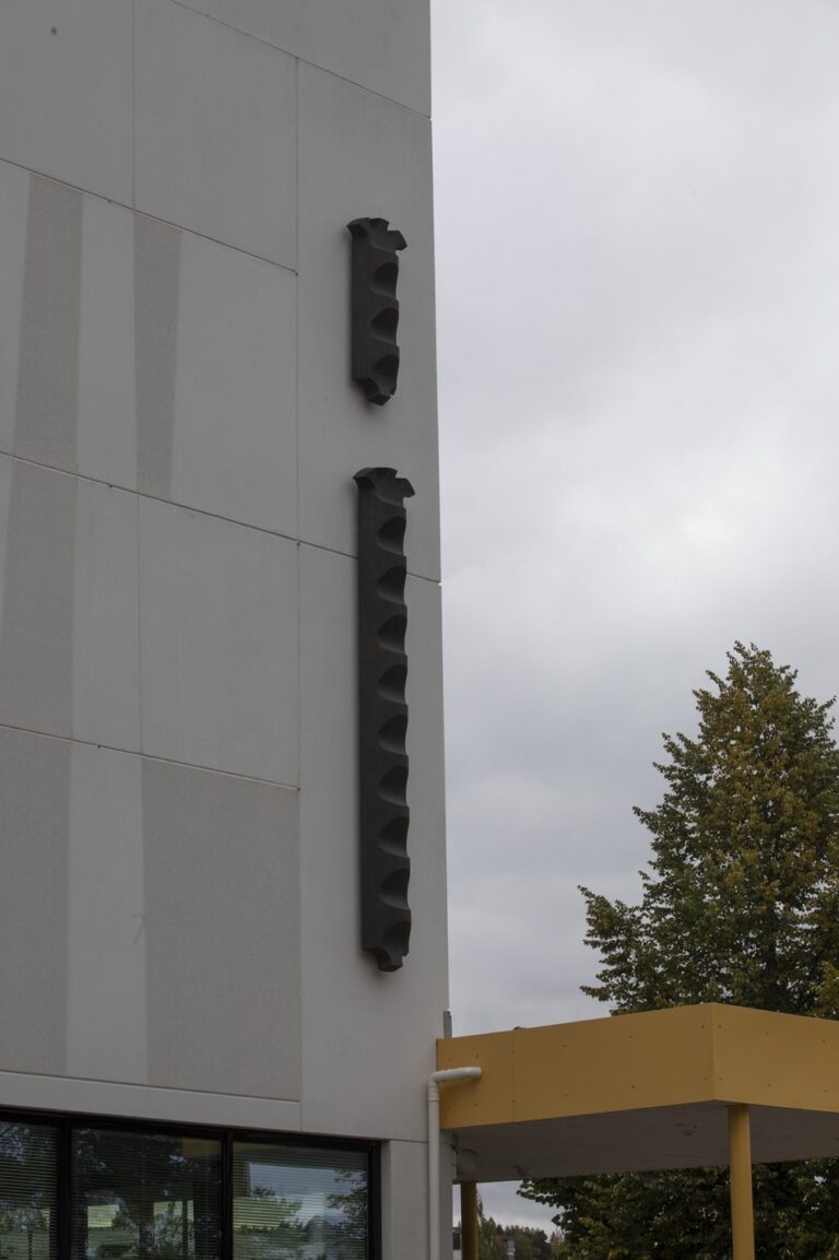 Attached to the wall of the building is a bronze sculpture depicting two vertical, narrow staircases, with one at the bottom and three sculptural spurs at the top.