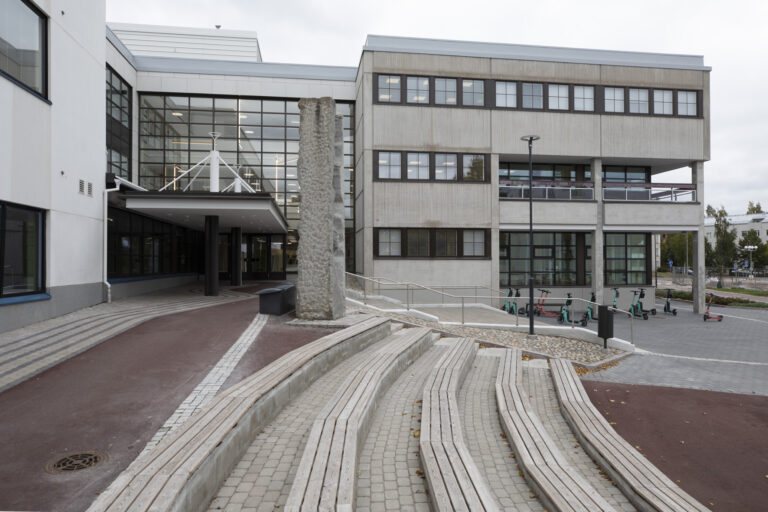 A tall, square stone slab placed in front of the building, at the top of the stairs.